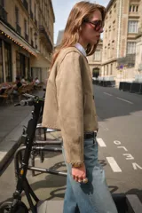 Chaqueta color tostado con efecto ante, cuello redondo y manga larga. Presenta detalles de acabados trenzados en el cuello, el cierre frontal, los puños y el bajo. Cuenta con cierre frontal de botones y bolsillos delanteros de vivo.