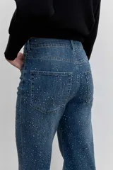 Pantalón de jean corte wide leg, color azul medio, con detalle de strass aplicado en toda la superficie frontal. Cuenta con tiro medio, cierre frontal con botón y bolsillos laterales y traseros.