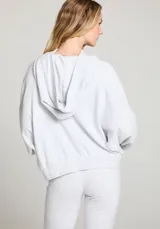 Hoodie gris jaspeado con capucha y mangas amplias. Estampado frontal con la palabra "Sunday" en azul y un sol naciente en naranja.