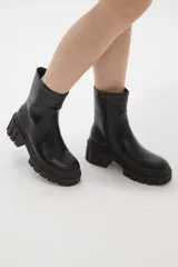 Bota de caña media en cuero sintético color negro, con suela track dentada y cierre lateral interno.