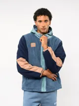 Campera de polar con capucha, cierre frontal completo y diseño en bloques de color azul y azul marino. Presenta detalles en nylon en la zona del cierre y la capucha, con logo de la marca aplicado en el pecho.