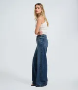 Pantalón wide leg de jean azul, tiro medio, con bolsillos funcionales, trabillas y tachuelas metálicas decorativas a lo largo de los laterales. Cierre frontal con botón y cremallera.