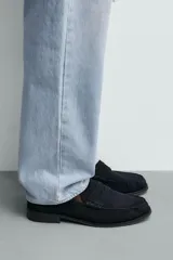 Mocasín de vestir para hombre, fabricado en piel con acabado en serraje de color azul marino. Presenta un diseño clásico con detalle de antifaz en el empeine, horma redonda, costuras visibles en el contorno y una suela sutil con ligero tacón.