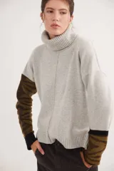 Polera de calce relajado con cuello alto, confeccionada en lana. Presenta un diseño bicolor con cuerpo en gris claro y mangas con estampado jacquard de arabescos en tonos tierra y negro. Incluye detalle de costura central vertical en el frente.