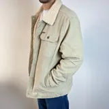 Chaqueta de pana color beige con forro de corderito en el cuello y el interior. Tiene cierre con botones, bolsillos en el pecho y bolsillos laterales.