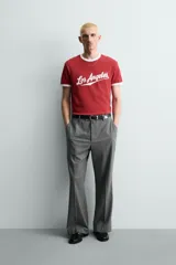 Camiseta roja de corte regular fit, con cuello redondo y mangas cortas. Presenta un estampado frontal con la frase "Los Angeles" en blanco y acabados de vivo en contraste blanco en cuello y mangas.