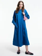 Vestido largo azul de algodón, con cuello mao, mangas largas y corte evasé. Presenta pechera con botones y bolsillos laterales. Ideal para uso casual en verano.