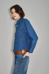 Camisa crop de denim azul, con cuello camisero, botones frontales dorados, dos bolsillos en el pecho y mangas abullonadas.