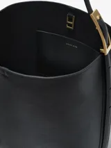Cartera tipo shoulder bag de cuero color negro, con diseño estructurado, correa ajustable para el hombro con hebilla metálica dorada y el logotipo de la marca grabado en dorado en la parte inferior.