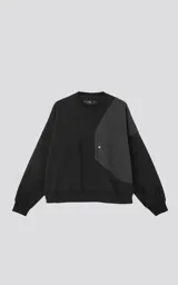 Buzo de cuello redondo, color negro, confeccionado en frisa gamuzada de algodón con recortes en microfibra, creando un efecto de capas. Presenta un bolsillo frontal tipo parche con cierre a presión.