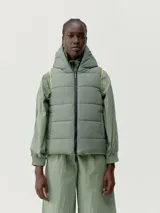 Chaleco acolchado reversible con capucha, cierre frontal de cremallera y bolsillos laterales. Diseño cortavientos y funcional con relleno vegano.