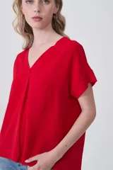 Blusa de poliéster color blanco con cuello en V, mangas cortas con dobladillo y corte holgado.