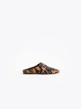 Mocasines destalonados tipo slide confeccionados en cuero vacuno con pelo en estampado animal print, con detalles en cuero negro, flecos frontales y un cierre metálico de torniquete.