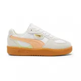 Championes Puma modelo Palermo, con diseño retro de perfil bajo. Presentan una base de cuero blanco con superposiciones de gamuza en tono crema, franja lateral característica en color naranja suave y detalles en verde claro. Incluye suela de goma color caramelo y logo Puma Palermo en dorado en el lateral.