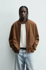 Cazadora bomber negra de corte regular fit, confeccionada en tejido efecto ante. Cuenta con cuello, puños y bajo en rib elástico, manga larga, bolsillos de vivo en la cadera y un bolsillo interior. Cierre frontal con cremallera.