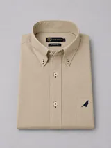 Camisa de algodón twill color beige, de corte clásico y manga larga, con cuello button-down, cierre frontal con botones y bolsillo en el pecho con detalle de ave bordada en azul marino.