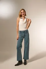 Pantalon de corte recto y tiro medio, confeccionado en denim color gris oscuro. Presenta bolsillos delanteros decorados con tachas metálicas pequeñas en los bordes y cierre frontal con botón y cremallera.