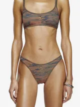 Bombacha de bikini de corte alto y estilo tanga, con estampado camuflado en tonos verde militar, marrón y azul. Confeccionada en tejido rib elástico reciclado, presenta un recorte metálico con el logo Oval D en el frente.