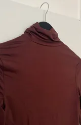 Top marrón de cuello alto y manga larga, con abertura en el abdomen y falda asimétrica.