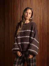 Buzo corto de tejido de punto en color negro, con diseño de textura en relieve y líneas horizontales blancas. Presenta cuello redondo y mangas largas con puños ajustados.