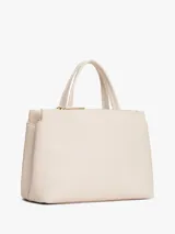 Cartera tipo satchel de Tommy Hilfiger en color beige, confeccionada en poliuretano con textura granulada. Presenta doble asa superior, correa ajustable extraíble, logo TH metalizado en el frente y dos franjas verticales decorativas con detalles entrelazados en rojo y negro.