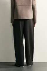 Pantalón de corte balloon fit en color gris oscuro, confeccionado en tejido con viscosa. Presenta pliegues frontales, cintura ajustable con cinturón integrado, bolsillos laterales y bolsillos traseros de doble vivo. Cierre frontal con cremallera y botón.