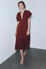 Vestido midi de color bordó con escote en pico y mangas cortas. Presenta un diseño con pinzas, cierre frontal con botones ocultos y un cinturón fino tipo cordón en el mismo tejido para ajustar a la cintura.
