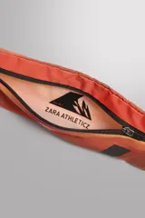 Riñonera deportiva técnica de color gris y negro, confeccionada en tejidos técnicos. Posee un compartimento principal con cierre de cremallera, bolsillos laterales planos (uno con mosquetón para llaves) y asa ajustable con hebilla de liberación rápida.