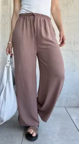 Pantalón marrón de tela texturizada, corte ancho, cintura elastizada con cordón ajustable y botones decorativos en los laterales.