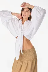 Top blanco de manga larga con diseño abullonado, cuello camisero, cierre frontal con botones y nudo ajustable en la cintura. Con textura sutil en la tela.