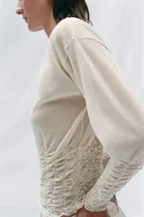 Jersey de punto semitransparente color crudo con cuello redondo y mangas largas, con detalles de nido de abeja elástico en el cuerpo y los puños.