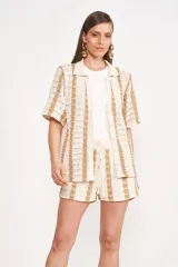 Camisa beige de tejido crochet a rayas verticales color dorado, con cuello camisero y mangas cortas.