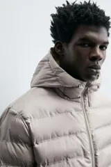 Campera puffer acolchada de corte regular fit en color negro, confeccionada en tejido técnico repelente al agua. Presenta cuello subido con capucha, cierre frontal de cremallera, mangas largas con puños elásticos y bolsillos laterales de vivo.