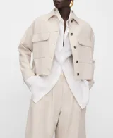 Chaqueta corta de algodón y lino color beige, de cuello italiano, manga larga con botones en los puños, cierre frontal de botones y bolsillos de plastrón con solapa en el delantero.