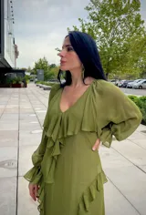 Vestido midi de gasa color verde oliva, con escote en V, mangas largas con puños elásticos y detalle de volados en la falda con abertura lateral.
