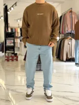 Sweater de punto color marrón, de manga larga, con textura acanalada y texto bordado en la espalda.