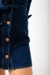 Vestido camisero corto de denim azul oscuro, con cuello clásico, mangas 3/4 con puños abotonados, cierre frontal con botones color cobre, cinturón de lazo y bolsillos con solapa en el pecho.