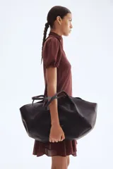 Vestido corto color marrón oscuro, con cuello alto y lazo frontal. Presenta mangas cortas abullonadas y una falda con vuelo y pliegues.