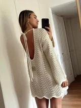 Vestido corto de tejido calado con patrón de ondas, confeccionado en algodón y lurex. Presenta mangas largas, cuello redondo y diseño holgado.