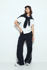 Pantalón babucha negro de silueta amplia y caída relajada, con detalle de líneas blancas laterales y cintura elastizada.