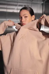 Buzo oversize color nude confeccionado en frisa, con capucha amplia, bolsillo canguro, terminaciones de puño y ruedo con rib, y logo de la marca bordado en el centro delantero.
