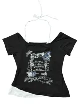 Remera negra con diseño ajustado de manga corta y escote off-shoulder, que incluye un detalle superpuesto simulando una bikini blanca por debajo. Posee estampado gráfico al frente con motivos florales y texto.
