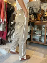 Bombacha de campo color beige, confeccionada en acrocel de algodón, con corte unisex de tiro medio. Presenta detalles de tela estampada con diseño floreado en la cintura, bolsillos, puños y una franja lateral a lo largo de la pierna. Cuenta con cierre reforzado y botón de madera.