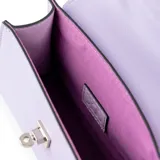 Cartera chica tipo bandolera de símil cuero color lila, con solapa, asa fija y correa regulable y desmontable. Cuenta con herrajes plateados y cierre de broche frontal.