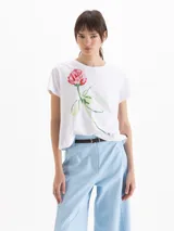 Remera blanca con estampado frontal de flor pintada al estilo acuarela, de manga corta y cuello redondo.