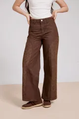 Pantalón de jean color marrón con diseño de paneles laterales estampados con motivos florales. Presenta un corte recto y holgado, con tiro medio y cierre frontal.