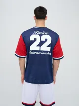 Remera de fútbol Umbro del Club Nacional de Football, de diseño tricolor con cuerpo azul marino, mangas y canesú rojos, y cuello en V con detalles en blanco y azul. Incluye el logo de Umbro en el pecho derecho y el escudo del club en el izquierdo.