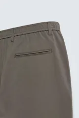 Pantalón de corte slim fit confeccionado en tejido elástico, con cintura elástica, cierre frontal con cremallera y botón, bolsillos laterales y bolsillos traseros de vivo.