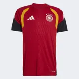 Camiseta de entrenamiento Adidas Tiro para el equipo nacional de Alemania, color rojo con detalles en amarillo y negro en los hombros y mangas. Presenta el escudo de la federación alemana con cuatro estrellas y el logo de Adidas en blanco. El tejido tiene un patrón texturizado y tecnología Climacool.