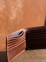 Billetera de cuero vacuno color marrón, con diseño plegable y logo de la marca grabado en el frente.